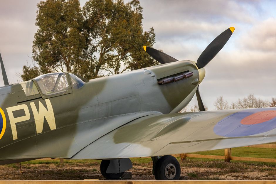 Close-up view of the front fuselage of a vintage military aircraft, showing a roundel insignia with a yellow outer ring, a blue middle ring, and a red central circle, painted on a grey metallic surfac